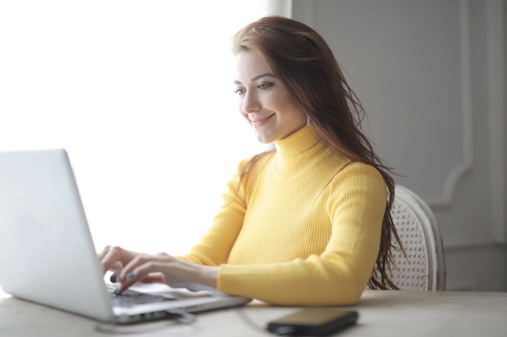 Femme portant un col roulé jaune, en face d’un ordinateur ouvert. Elle est en train de taper quelque chose sur le clavier.