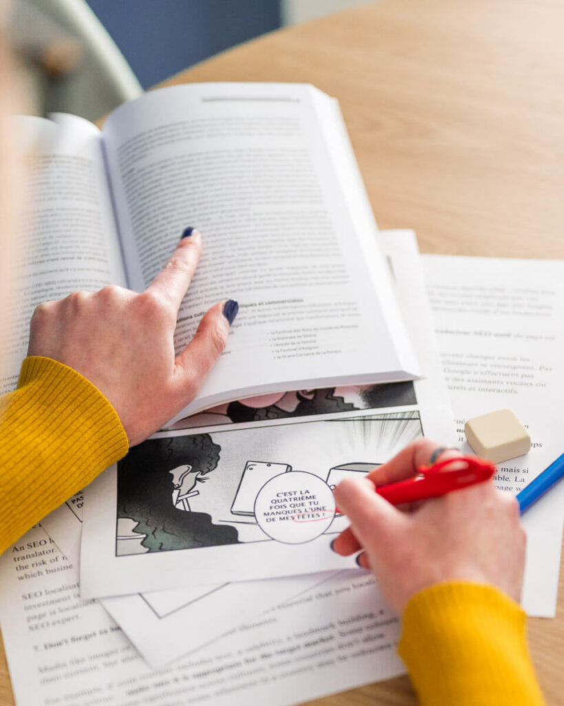 Correcteur professionnel qui corrige un manga en français à l'aide un stylo rouge et d'un livre de référence.
