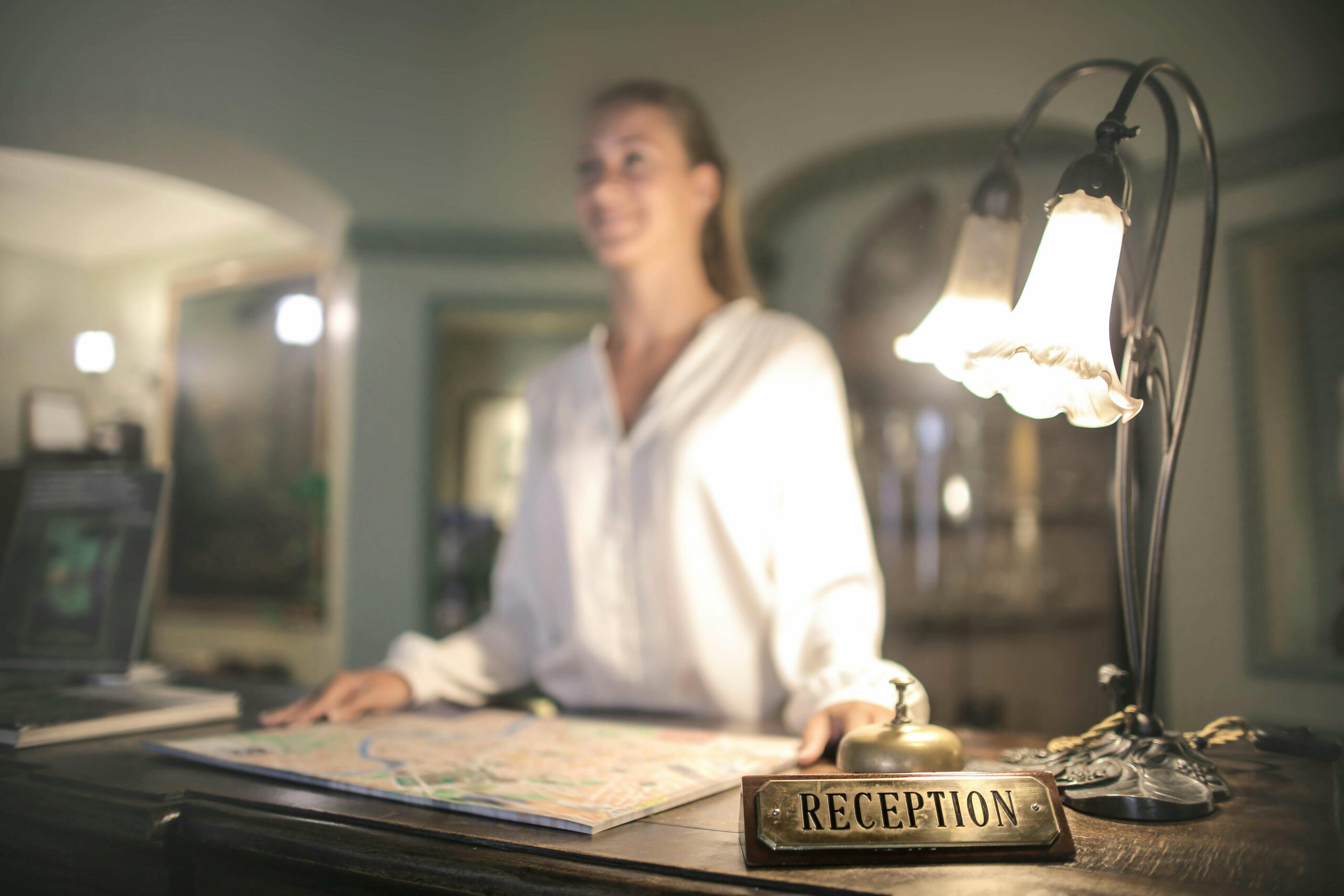 Une réceptionniste accueille des touristes dans un hôtel frontalier. Une carte de la ville est posée sur le comptoir.